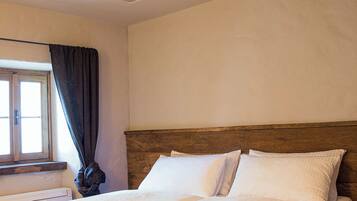 A bedroom with a wooden headboard, white bedding, a fur throw, and a window with curtains.