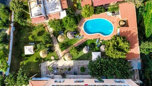 An aerial view of a hotel with a swimming pool surrounded by greenery, a rooftop terrace, and a parking area. - HARMONY HOTEL AND STUDIOS (Hersonissos)