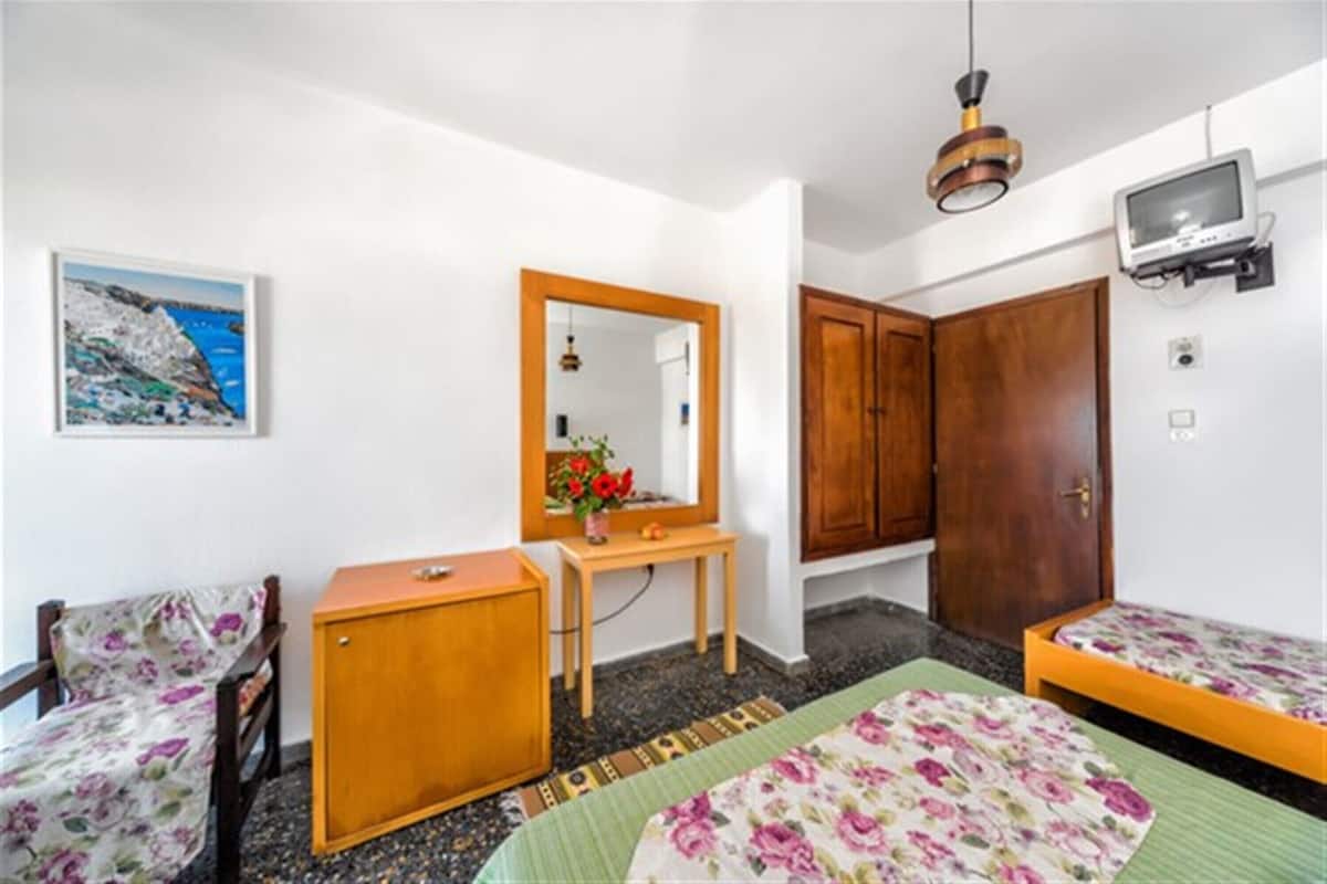 A bedroom with a bed, a wooden cabinet, a small table with a mirror, a television mounted on the wall, and a painting on the wall.