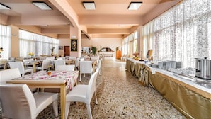 A spacious dining area with multiple tables and chairs, a kitchen counter, and large windows with patterned curtains. - HARMONY HOTEL AND STUDIOS (Hersonissos)