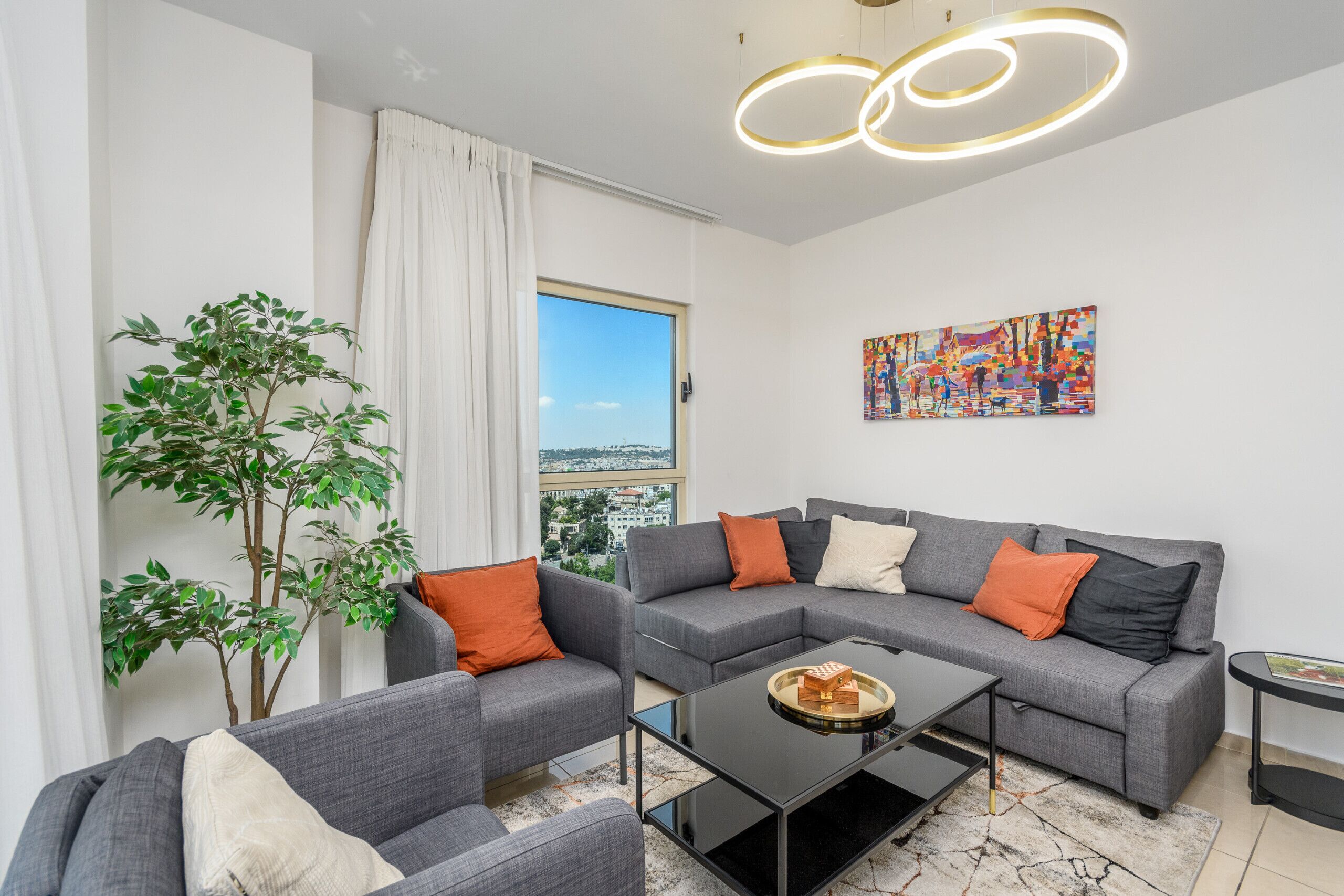A modern living room with grey sofas, a coffee table, and a large window with a view of the city.