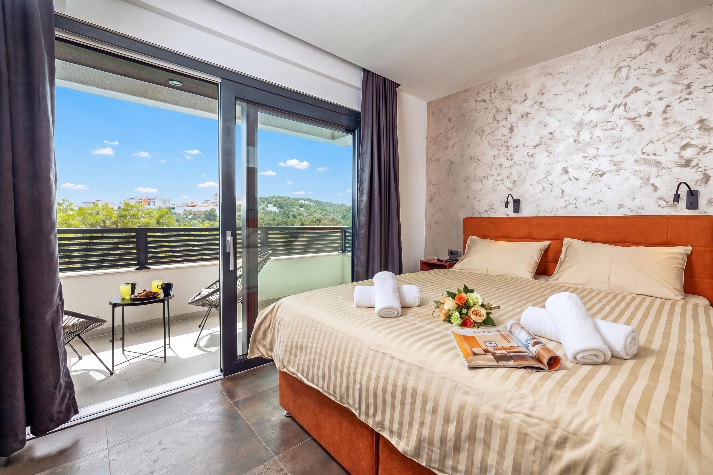 A hotel room with a large bed, a balcony with a table and chairs, and a view of the city.