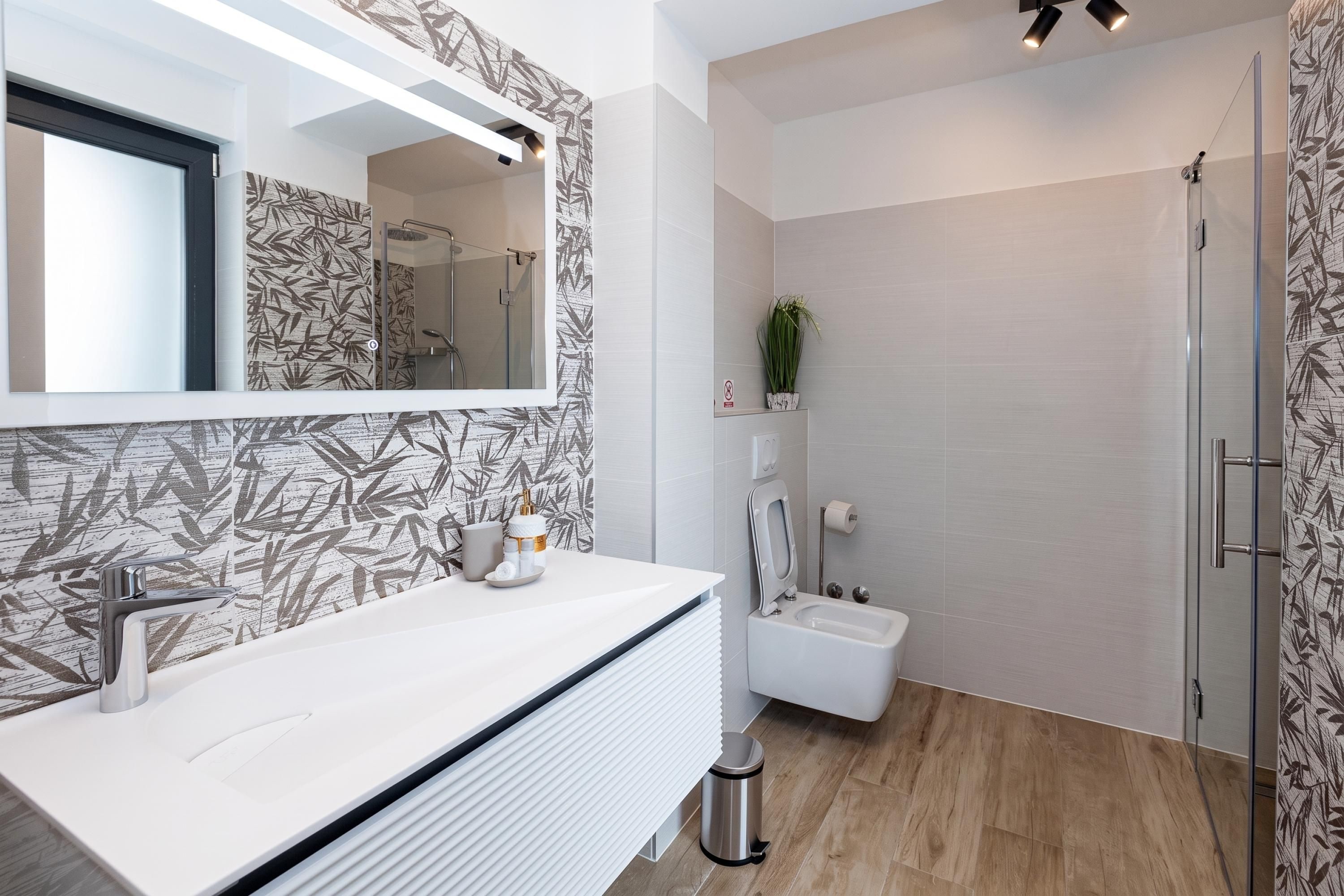 A modern bathroom with a white vanity, a glass shower enclosure, and a bamboo-patterned wall.