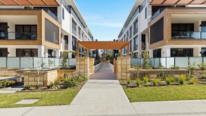 A modern apartment building with a central courtyard, stone walls, and a covered walkway. - Allura Escapes by Experience Jervis Bay (Huskisson)
