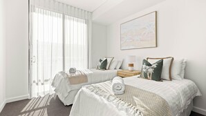 A hotel room with two beds, a large window with sheer curtains, a bedside table with a lamp, and a painting on the wall. - Allura Escapes by Experience Jervis Bay (Huskisson)