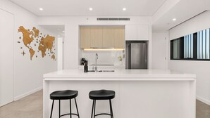 A modern kitchen with a white countertop, stainless steel appliances, and a world map wall decoration. - Allura Escapes by Experience Jervis Bay (Huskisson)