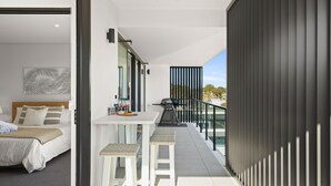 A modern bedroom with a bed, a small table with a bottle and glasses, and a balcony with a grill. - Allura Escapes by Experience Jervis Bay (Huskisson)