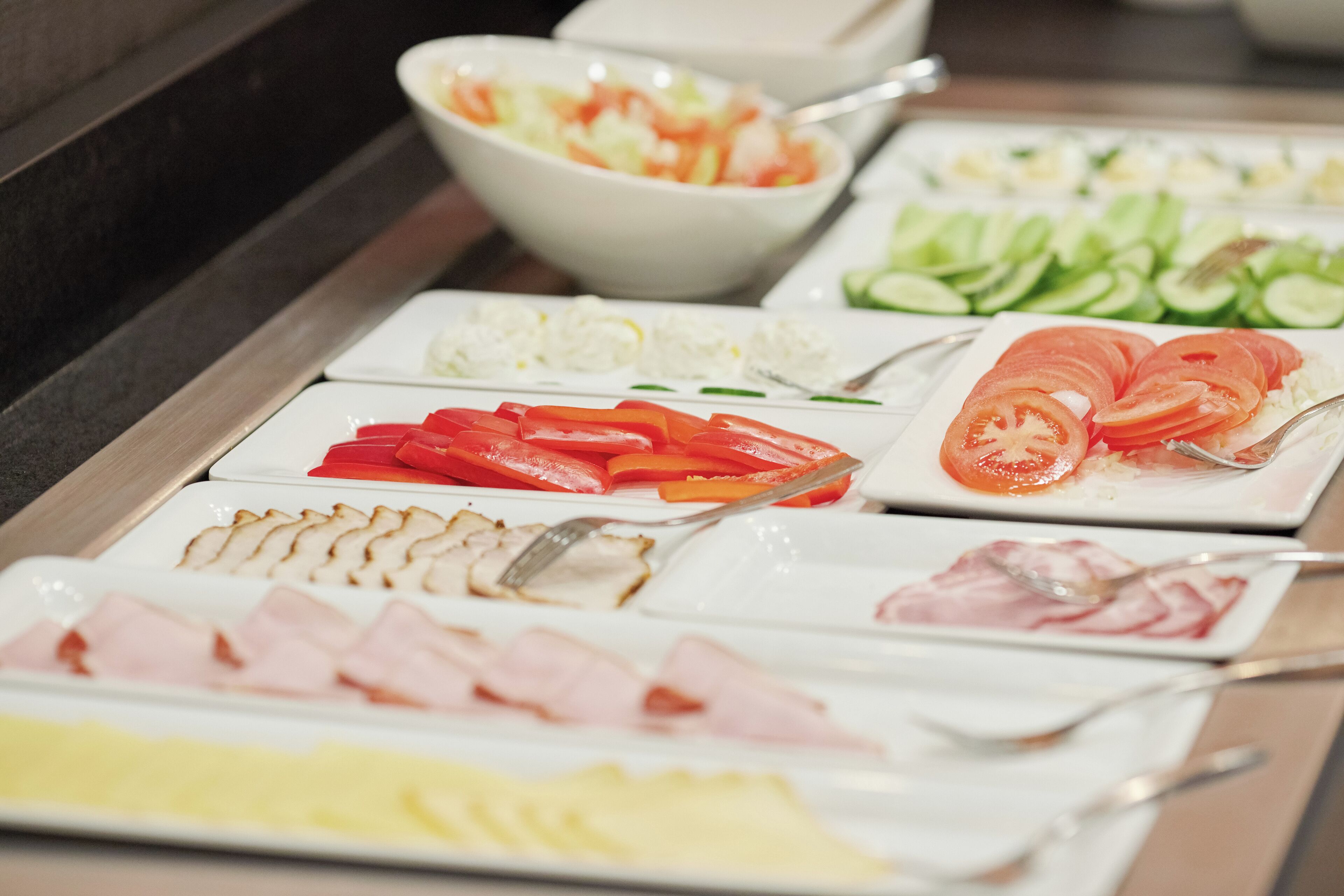 Un bufé con diversas opciones de comida, incluyendo carnes en rodajas, verduras y ensaladas.