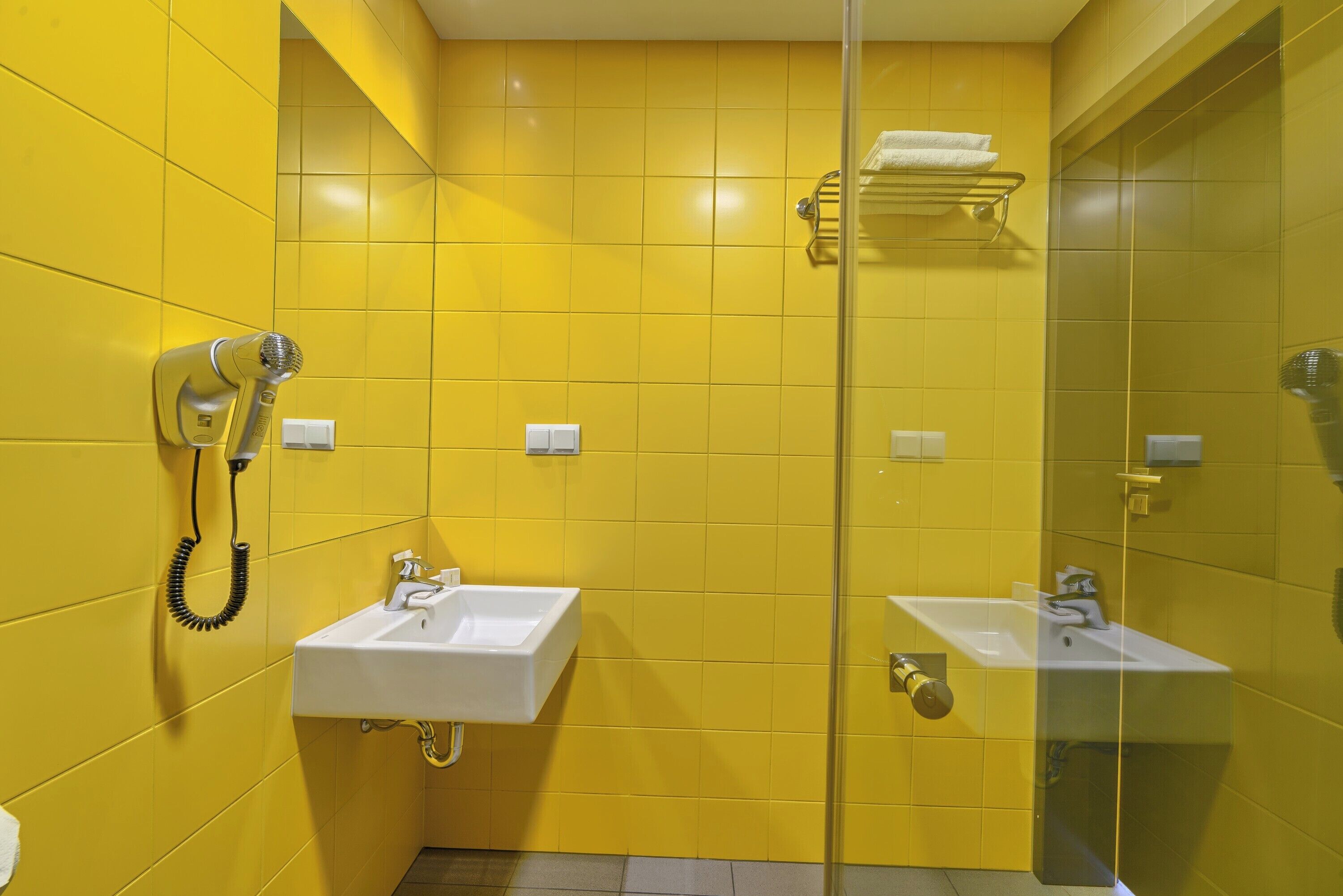 Een badkamer met gele wanden, twee wastafels, een haardroger en een handdoekhouder.