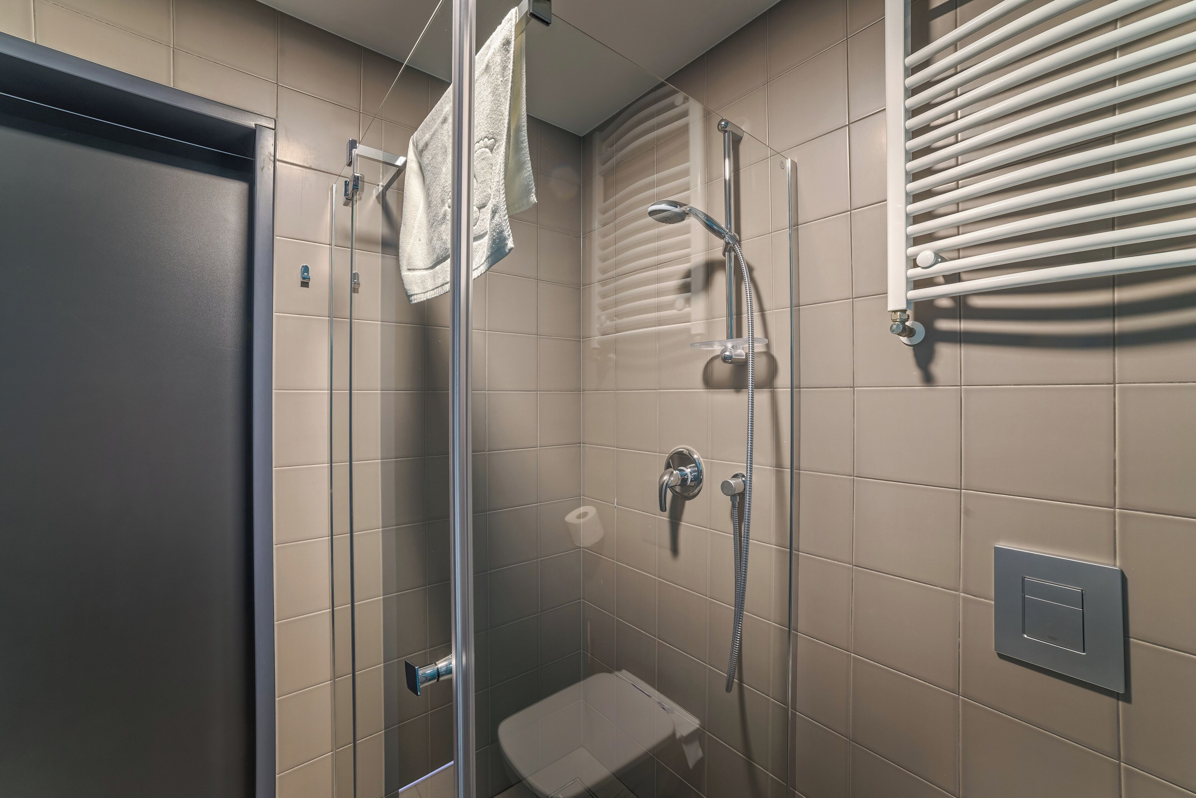 Una ducha moderna con puerta de vidrio, un cabezal de ducha manual y un perchero para toallas.