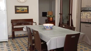 Een eetgedeelte met een tafel, stoelen, een kroonluchter, een koelkast, een spiegel en vloertegels met een patroon.