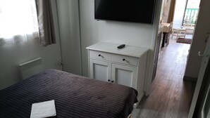 Un dormitorio con una cama, un aparador blanco, un televisor de pantalla plana y vistas al balcón.