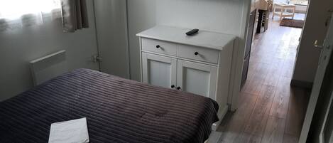 Een slaapkamer met een bed, een witte dressoir, een flatscreen televisie en uitzicht op het balkon.