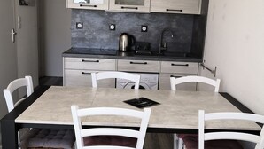 Una cocina moderna con comedor. Incluye una isla de cocina, sillas blancas y una cafetera.