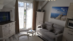 Una sala de estar moderna con un sofá, una mesa de comedor y un televisor. Hay una ventana con cortinas, un reloj y un cuadro en la pared.