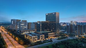 A modern high-rise building with a prominent vertical design, surrounded by other mid-rise buildings and a well-maintained urban landscape. - The Perennial Tianjin, A JdV by Hyatt Hotel (Tianjin)