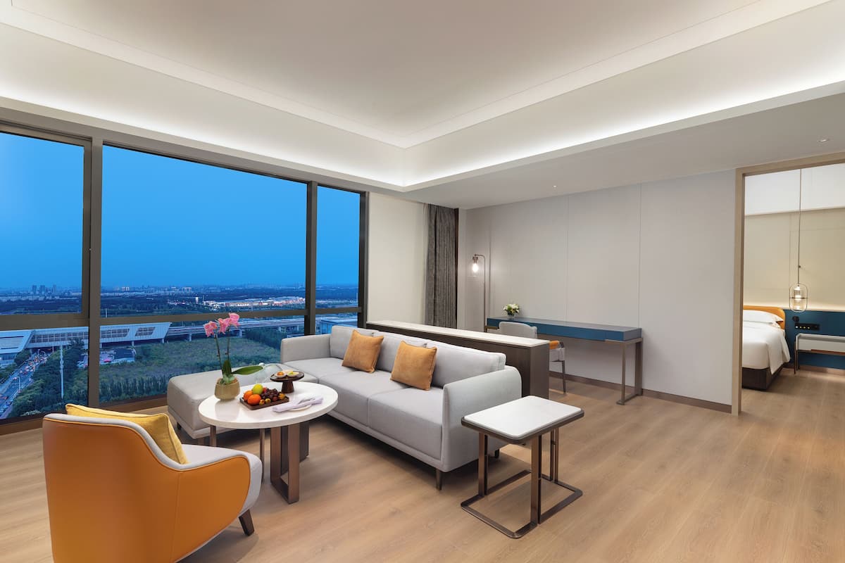 Een moderne hotelkamer met een groot raam, een bank, een eettafel en een kleine keukenhoek.