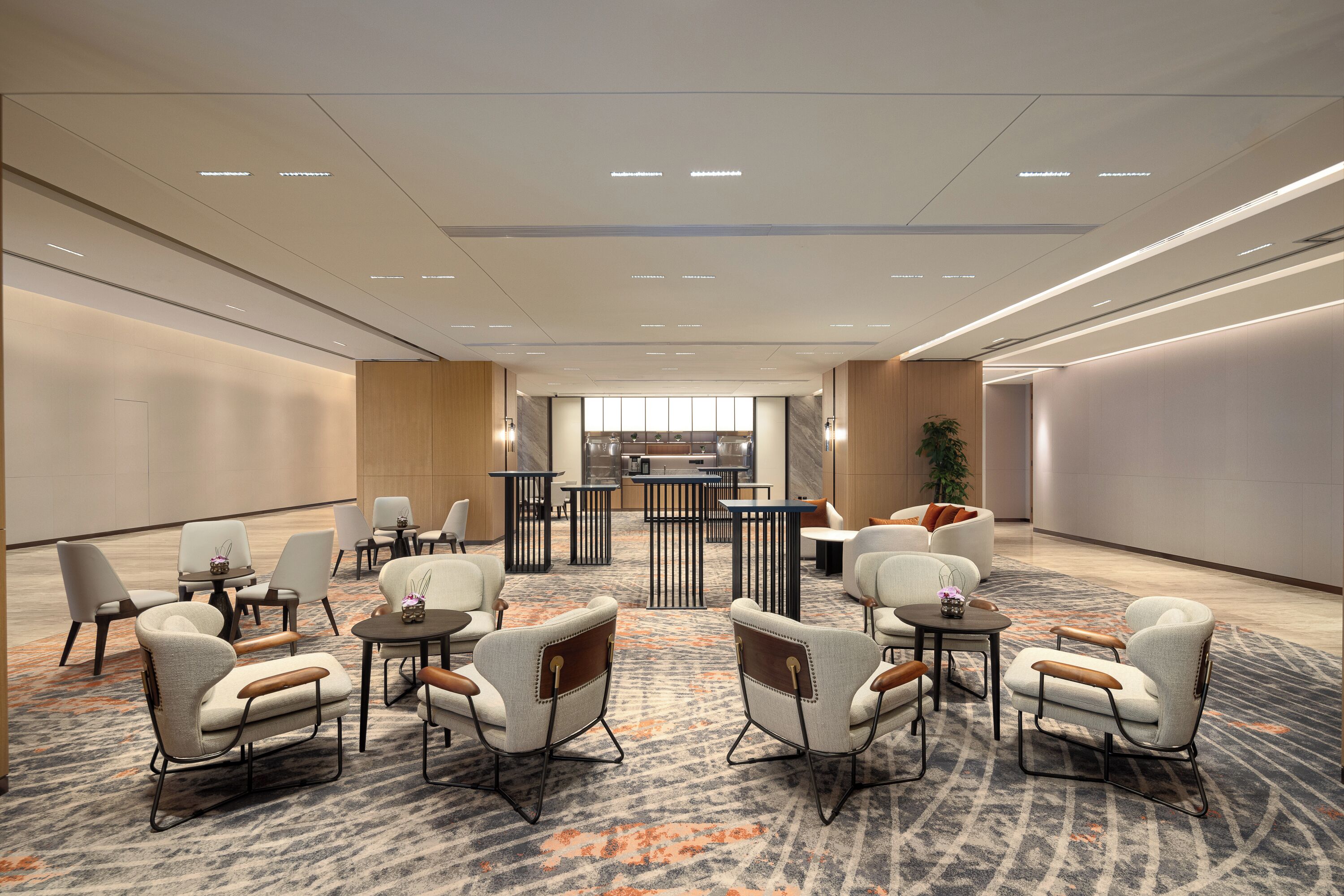 Un hall de hotel espacioso con muebles modernos, una zona de estar central y vistas a la cocina al fondo.