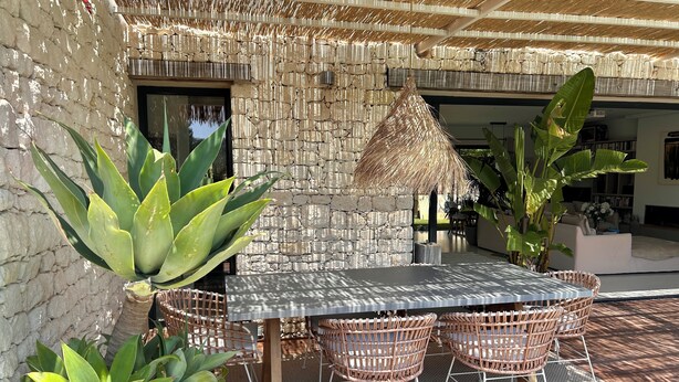 A patio with a stone wall, a woven table, wicker chairs, and large green plants. - Magnificent house on the Côte Bleue, 2 steps from the calanques! (Le Rove)