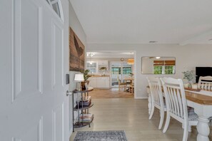 A dining area with a wooden table and white chairs, a kitchen in the background, and a white door on the left. - Southern Enchantment at Wilmington Isl -Savannah (Savannah)
