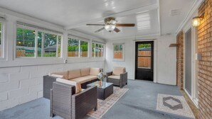 Un patio cubierto con mobiliario de mimbre, ventilador de techo y ventanas amplias.
