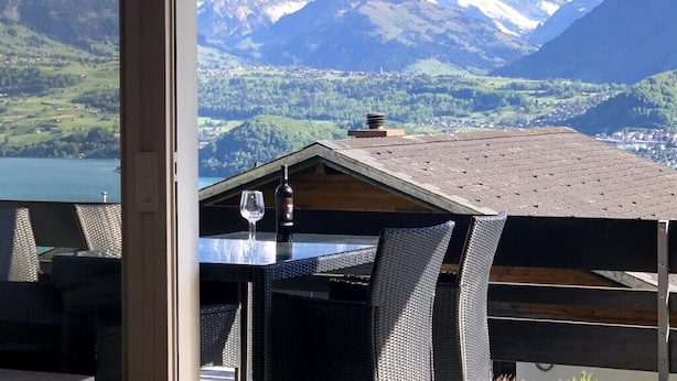 A dining area with a table and chairs, a bottle of wine, and a view of snow-capped mountains. - die Villa", Eine Wohnung für 6 Personen (Sigriswil)