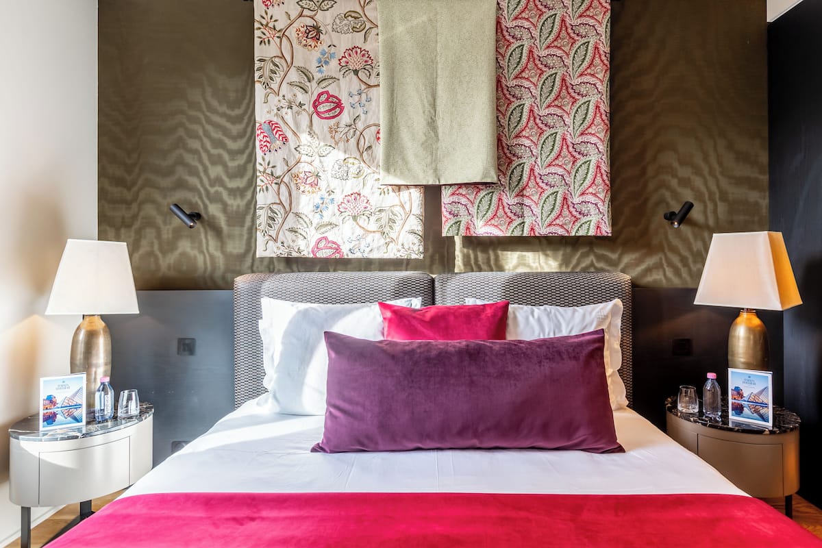 A hotel room with a bed, two bedside tables, lamps, a headboard, and patterned curtains.