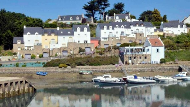 A coastal town with a marina, houses with gabled roofs, and a clear sky.