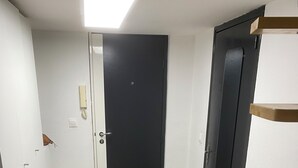 Une pièce avec un plancher en bois, une porte noire et un mur blanc sur lequel est fixé un téléphone.