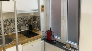 Une cuisine compacte dotée d’un plan de travail en bois, d’un évier, d’un petit réfrigérateur et d’une fenêtre avec une porte en verre dépoli.