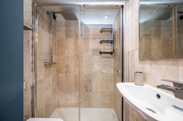 A modern bathroom with a glass-enclosed shower, a white bathtub, and a sink with a mirror.