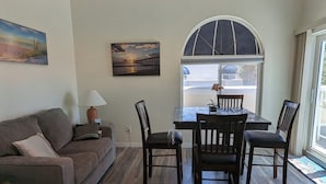 A living room with a sofa, a table with chairs, a lamp, and a painting on the wall. - Oceanfront 2br/2b, in Port Canaveral, Heated Pool & Spa, Ocean Views (Cape Canaveral)