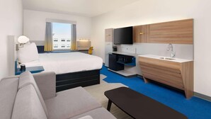 Quarto de hotel com cama, sofá, escrivaninha, televisão, micro-ondas e pia.