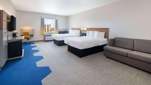 Quarto de hotel com duas camas, um sofá, uma mesa de escritório com computador e uma televisão.