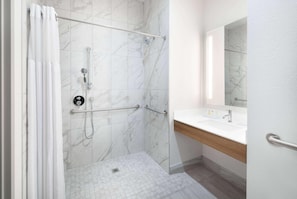 A bathroom with a shower, grab bars, a sink, and a mirror. - Microtel Inn & Suites By Wyndham Amarillo West (Amarillo)
