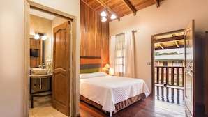 A bedroom with a wooden ceiling, a bed with a white quilt, a wooden door, and a view of an outdoor balcony. - Monteverde Country Lodge (Monteverde)