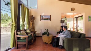 A reception area with a wooden reception desk, a green sofa, and a wicker ottoman. - Monteverde Country Lodge (Monteverde)
