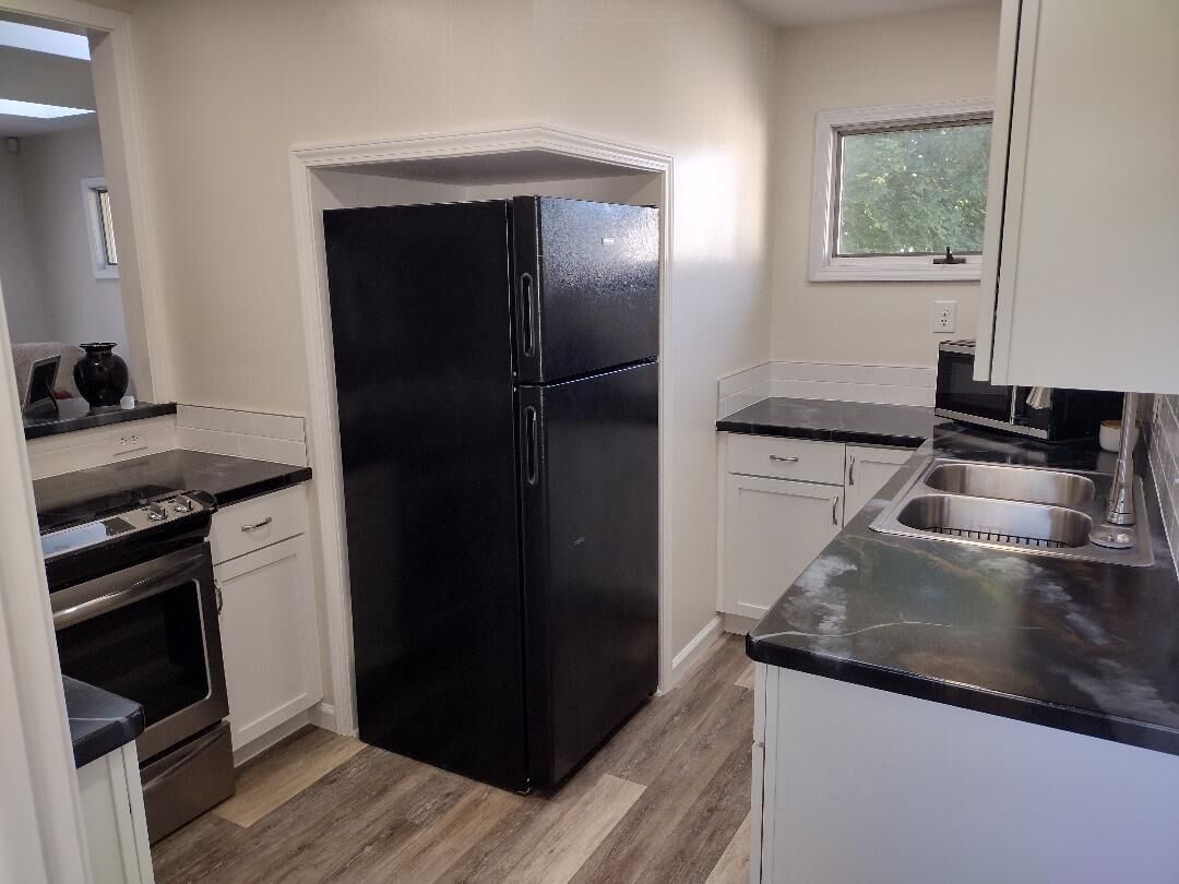Una cocina con refrigerador negro, pileta de acero inoxidable y muebles blancos.