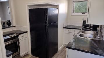Una cocina con refrigerador negro, pileta de acero inoxidable y muebles blancos.