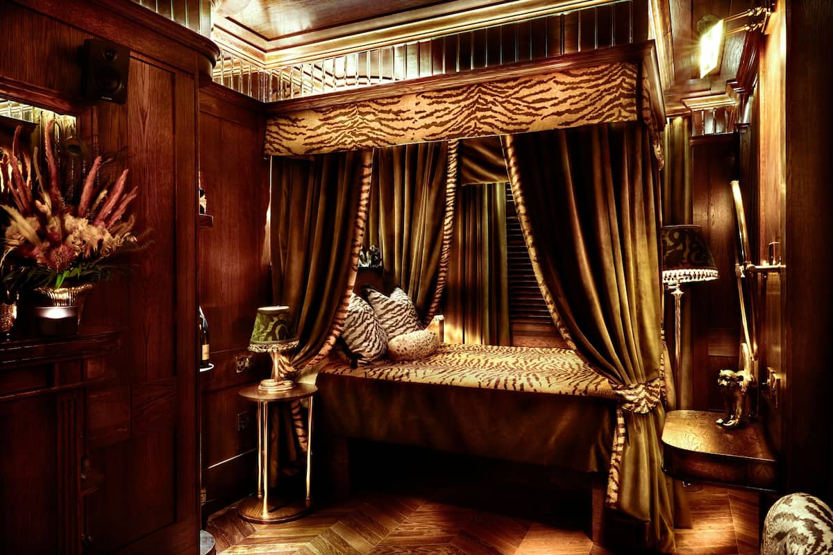 A luxurious bedroom with a canopy bed, a small table with a lamp, and a decorative plant.