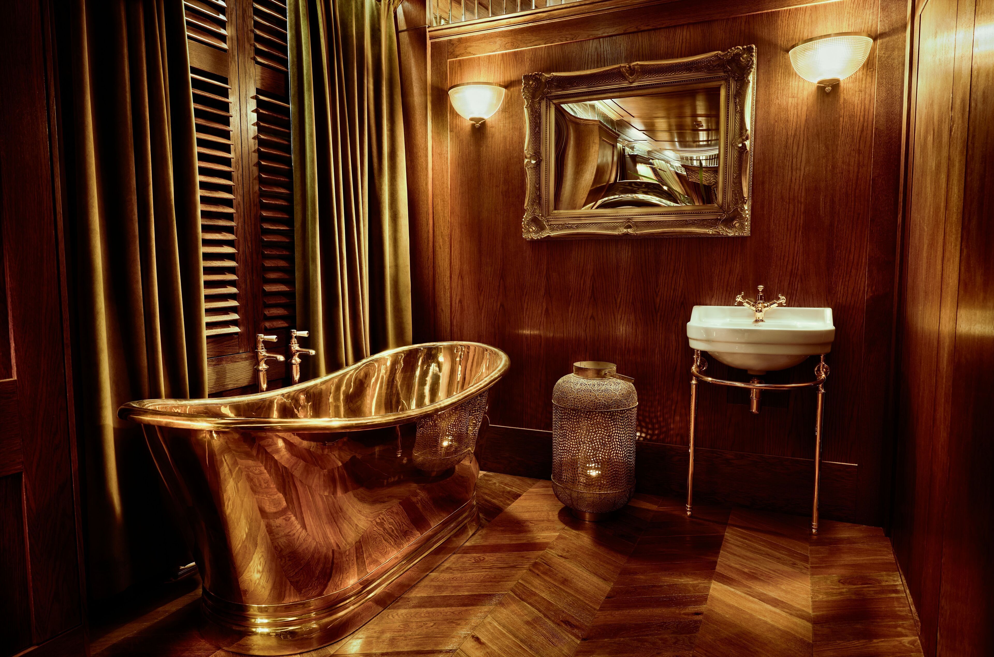 Une salle de bain classique en bois, avec une baignoire sur pieds, un lavabo sur colonne et un miroir doté d’un cadre décoratif.