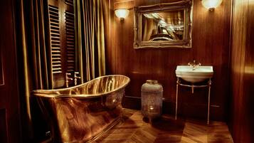 A classic wooden bathroom with a freestanding bathtub, a pedestal sink, and a mirror with a decorative frame.