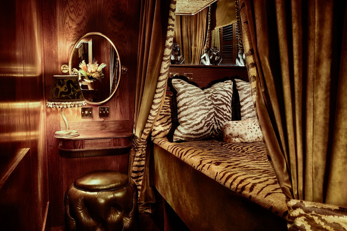 A bedroom with a bed, a vanity with a mirror, a lamp, and a small stool.