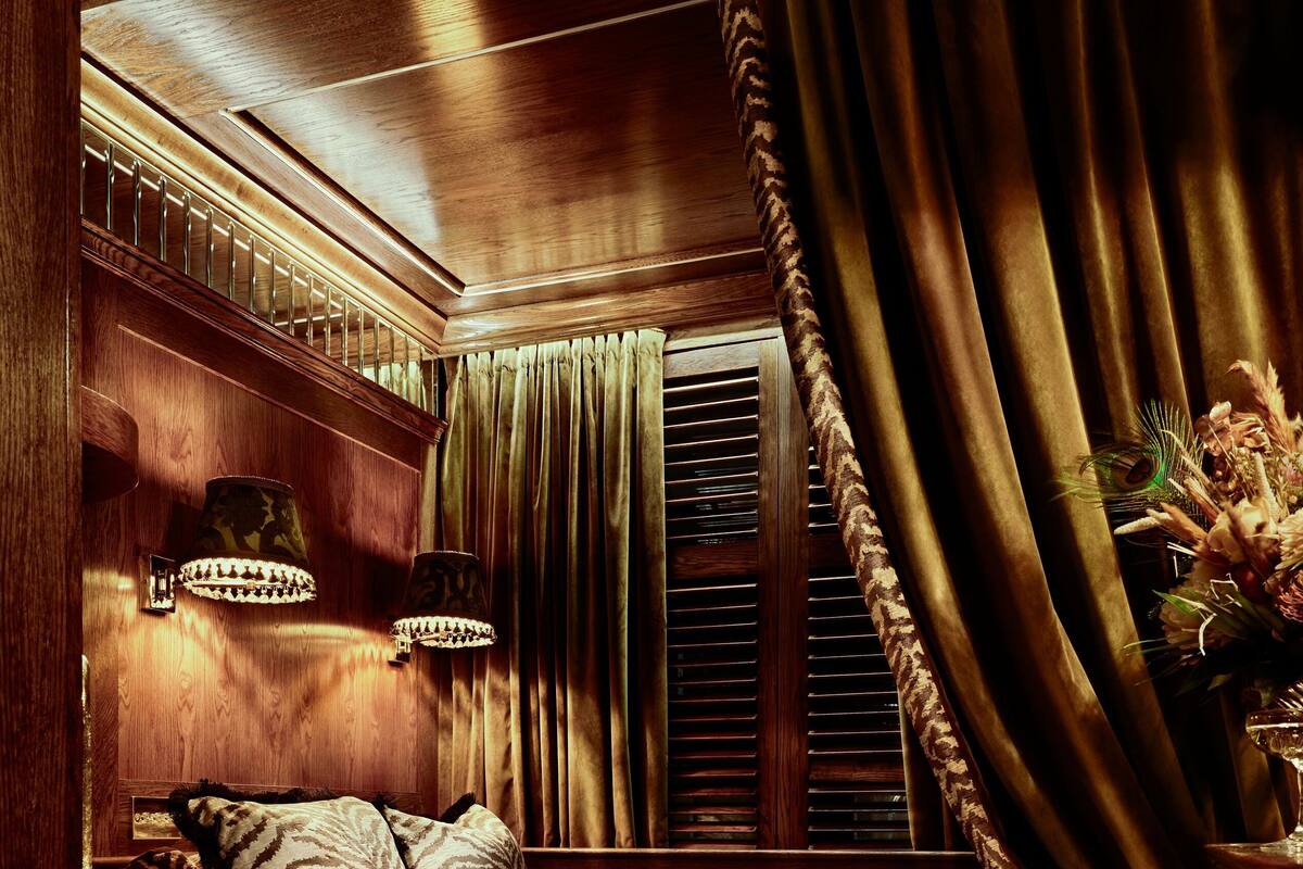 A cozy bedroom with a wooden headboard, a bed with patterned bedding, a nightstand, a lamp, and a decorative vase.