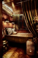 Un dormitorio acogedor con cabecera de madera, cama con ropa de cama estampada, mesita de noche, lámpara y un jarrón decorativo.