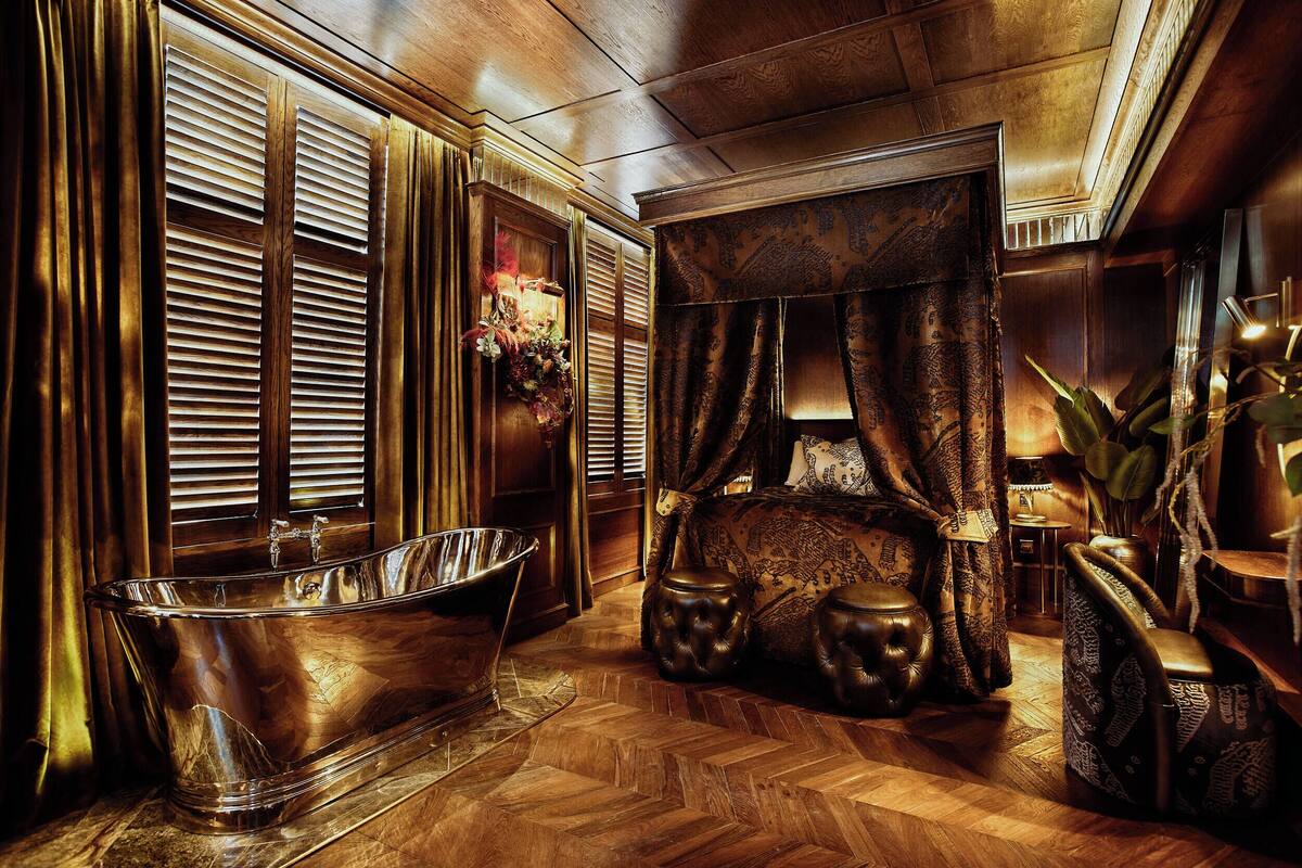 A luxurious bathroom with a freestanding bathtub, ornate curtains, and a wooden floor.