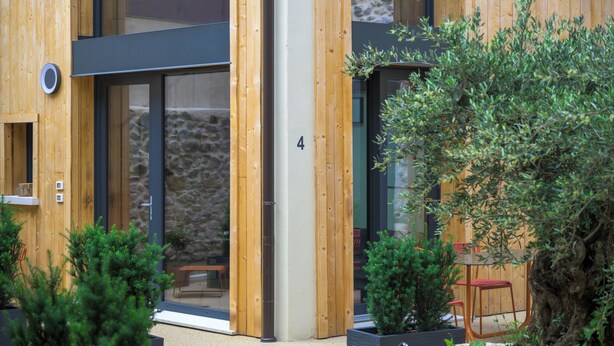 A modern building with wooden exterior walls, a stone wall, and a glass door. There are potted plants and a wooden bench outside. - Open space on two floors in detached cottage in ancient medieval courtyard (Solarolo)
