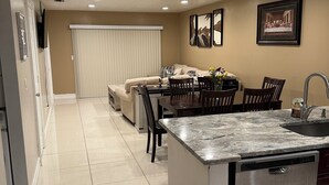 A modern kitchen with a central island, a dining area with a table and chairs, and a living area with a sofa. - Cozy 2-bedroom apartment in gorgeous Downtown Cape Coral with, Pool, AC, WiFi (Cape Coral)