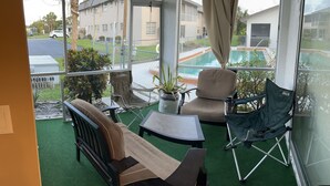 A balcony with a view of a swimming pool, a chair, a small table, and a potted plant. - Cozy 2-bedroom apartment in gorgeous Downtown Cape Coral with, Pool, AC, WiFi (Cape Coral)