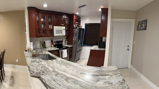 A kitchen with a marble countertop, wooden cabinets, a microwave, and a refrigerator. - Cozy 2-bedroom apartment in gorgeous Downtown Cape Coral with, Pool, AC, WiFi (Cape Coral)